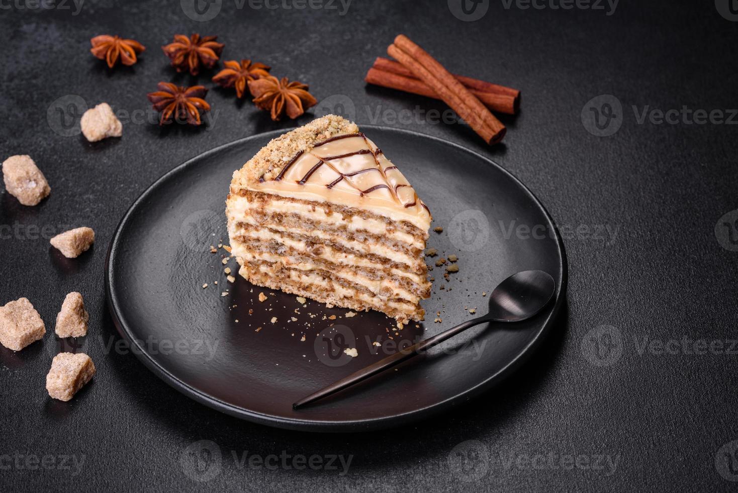 Esterhazy cake sliced on black plate close-up. Delicatessen sweet dessert with almond meringue dough and buttercream photo