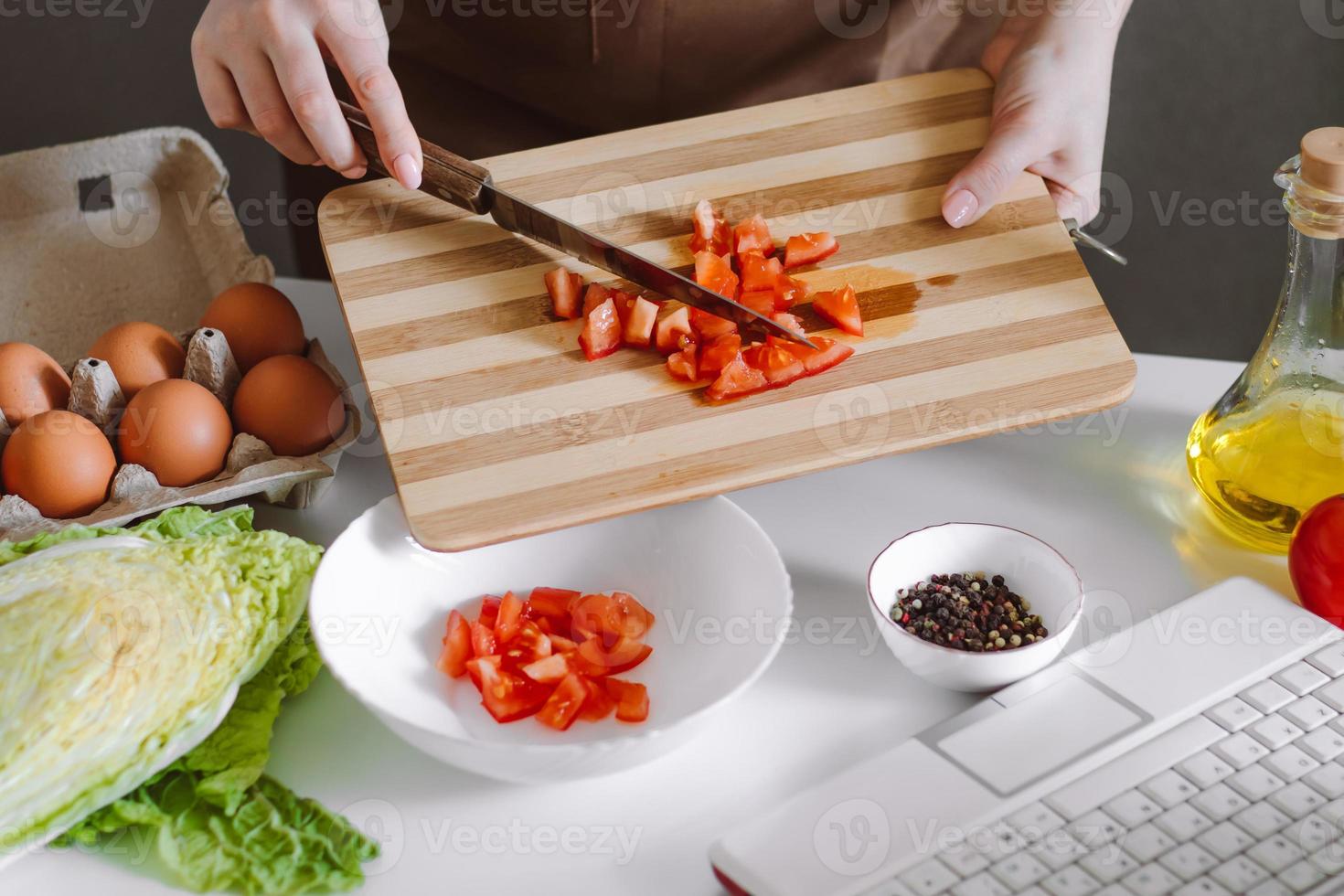 Woman blogger preparing diet vegetable salad. Online cooking lessons, using a laptop in the kitchen. Record cooking recipes on camera. photo