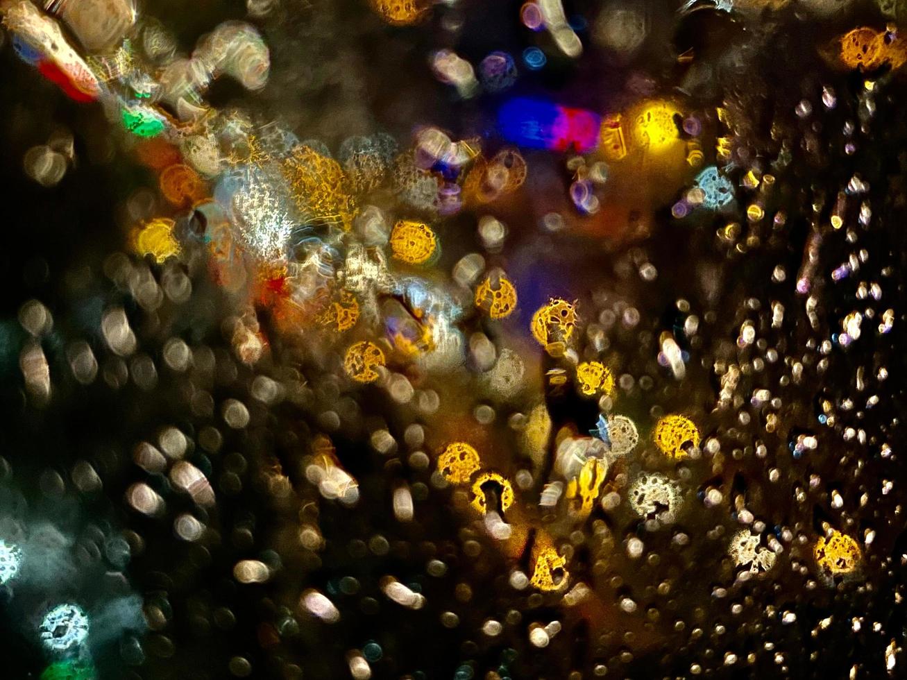 Shot through the glass in the rain with street lights and car headlights in the background. Blurred bokeh glitter of light background photo