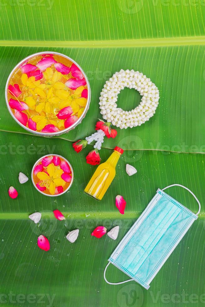 Songkran Festival background with jasmine garland Flowers in a bowl of water, perfume and limestone on a green wet banana leaf background. photo