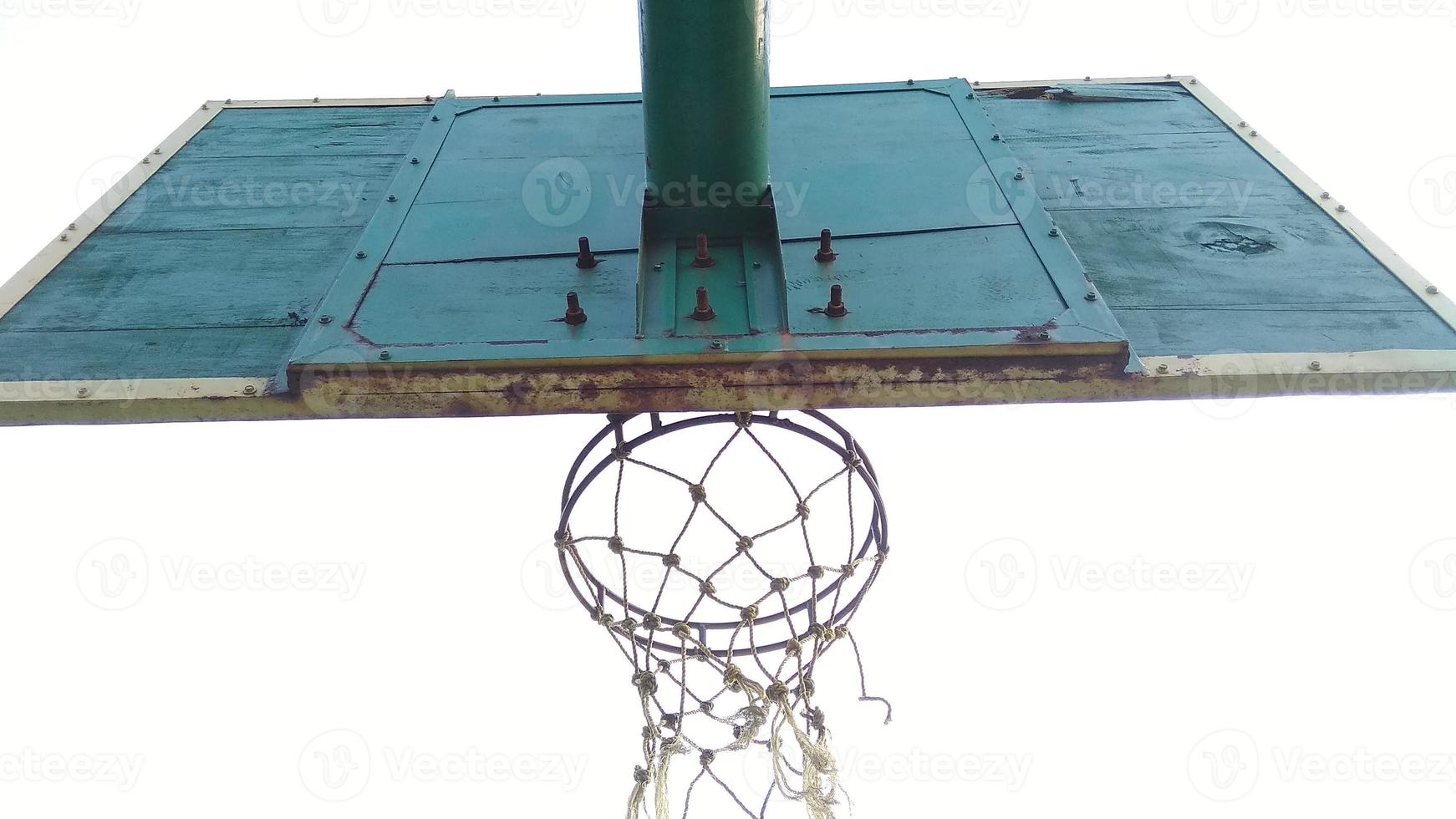 vista inferior del viejo aro de baloncesto verde tenue y red rota con un fondo oscuro del cielo matutino en el campo deportivo público. foto