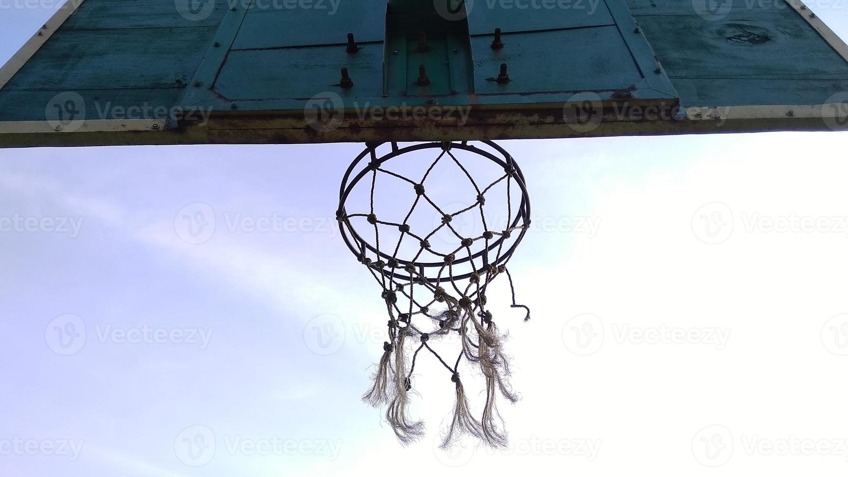 Bottom view of dim green old basketball hoop and broken net with a dark background of morning sky in the public sport field. photo