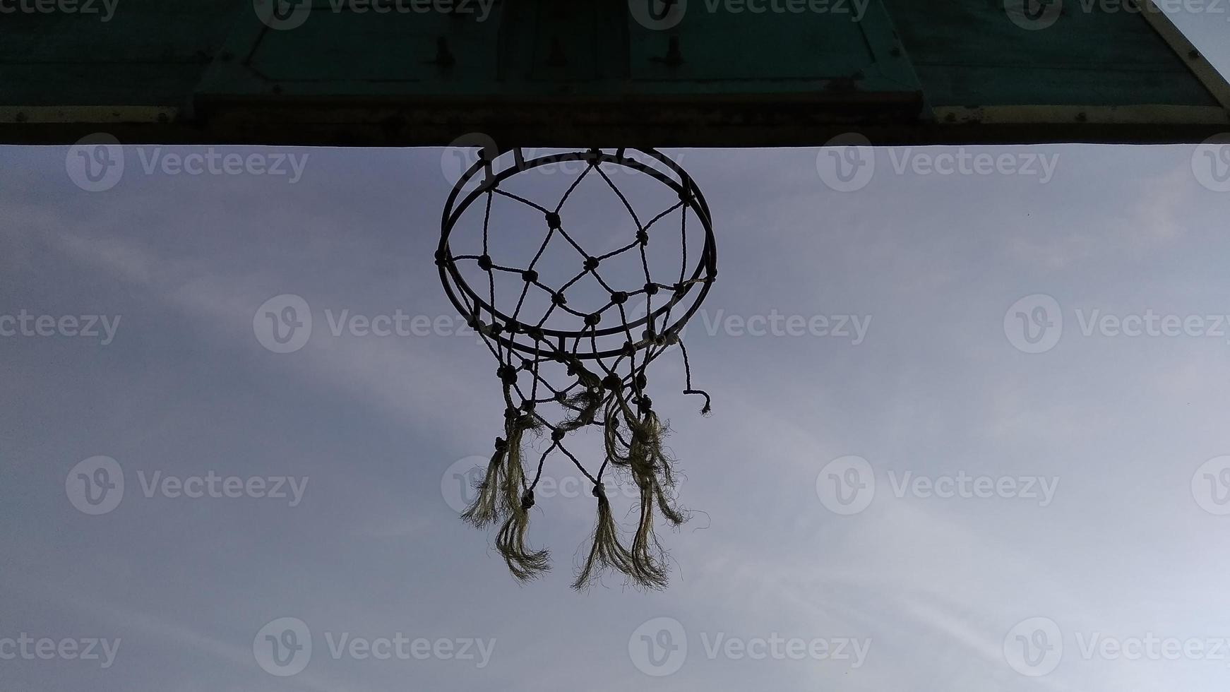 vista inferior del viejo aro de baloncesto verde tenue y red rota con un fondo oscuro del cielo matutino en el campo deportivo público. foto