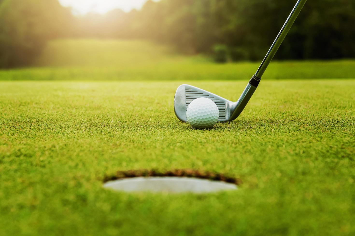 close up golf club and golf ball on green grass with sunrise background photo