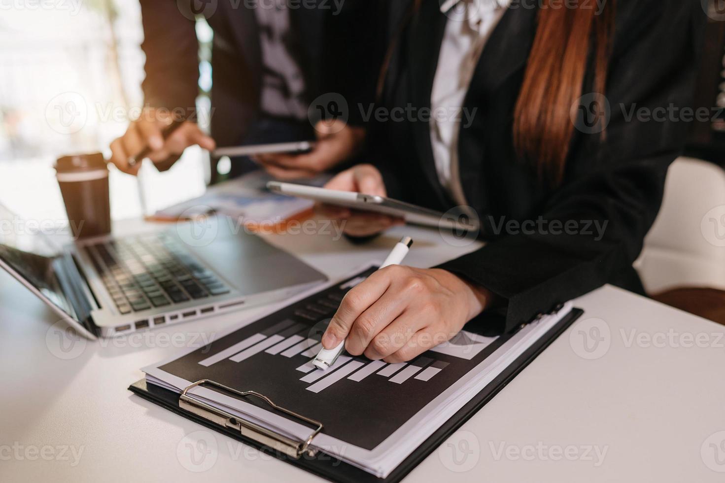 Businessman hand using laptop and tablet with social network diagram and two colleagues discussing data on desk as concept in morning light. photo