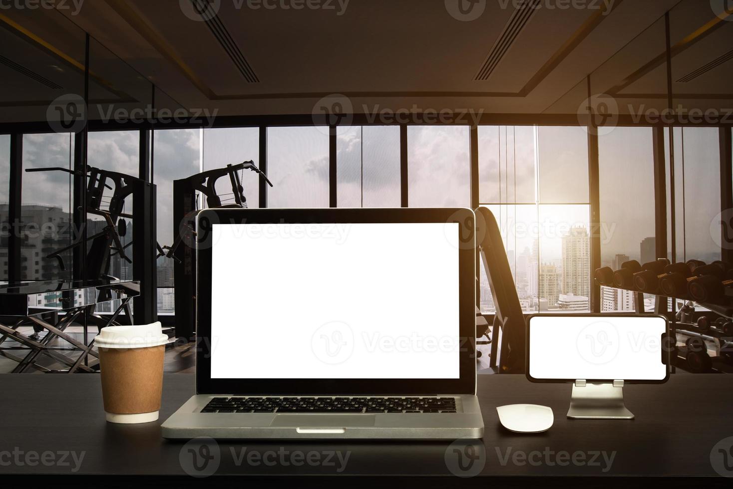 Front view of cup and laptop, smartphone, and tablet on table in Office in fitness gym in morning light photo