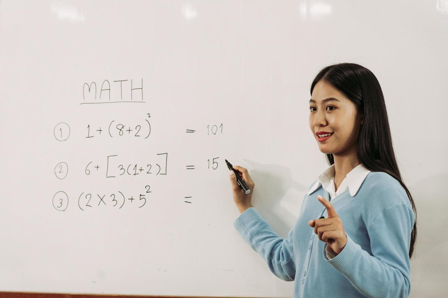 una profesora asiática está enseñando a los estudiantes en el aula mientras señala números en la pizarra blanca. foto