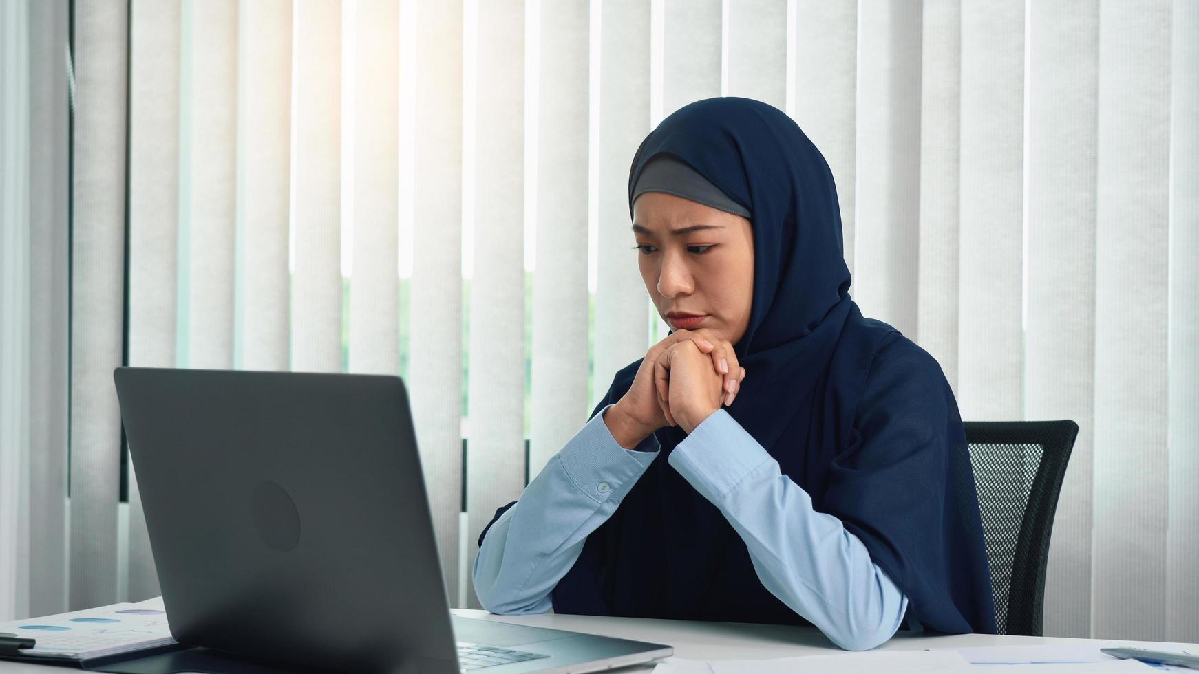Muslim woman looks at a computer screen and gets stressed. photo