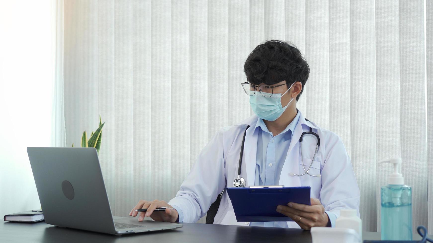 Doctor was sitting in the office working on a laptop computer while wearing a mask. photo
