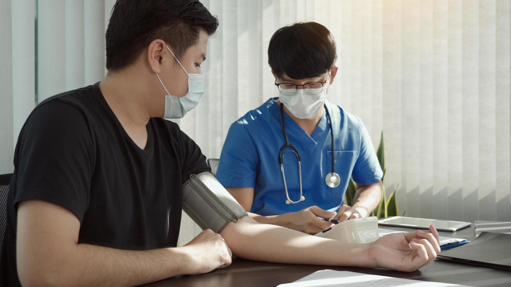 Asian doctor is using a patient's blood pressure monitor at the time of his annual check-up and explains his blood pressure. photo