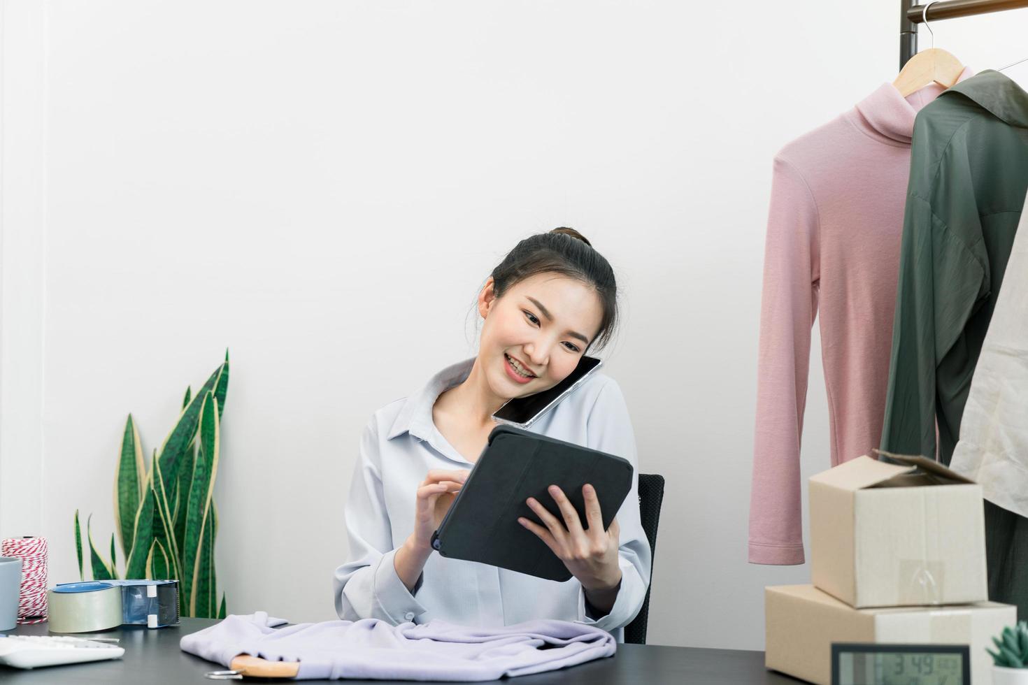 Asian entrepreneur talking on the phone with a customer while checking inventory on a tablet. photo