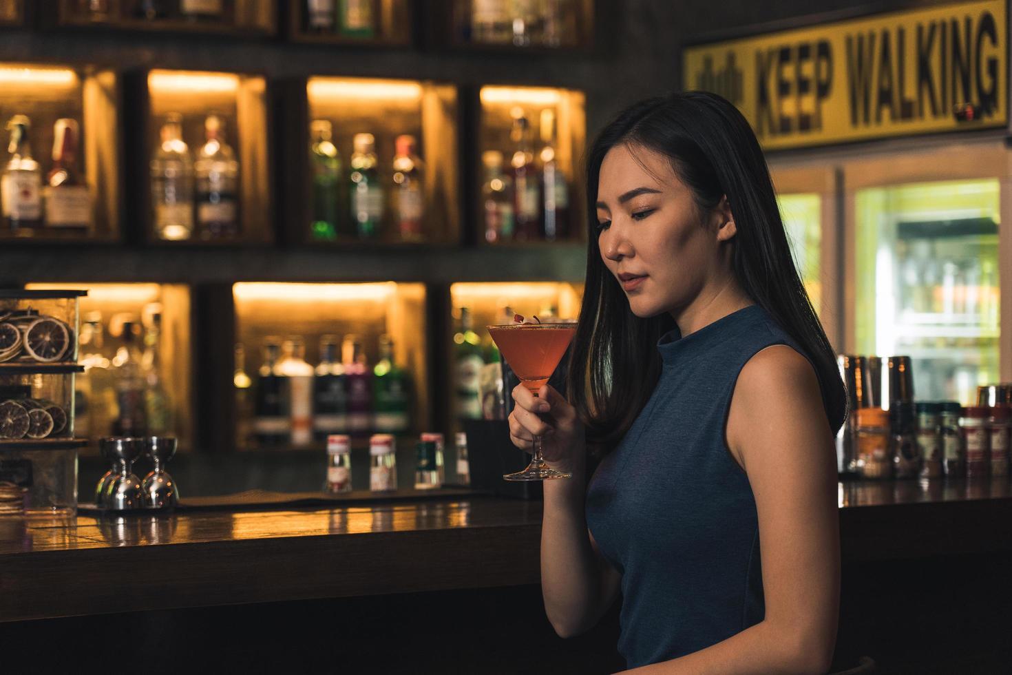 Asian woman drinking a cocktail at a bar at night. photo