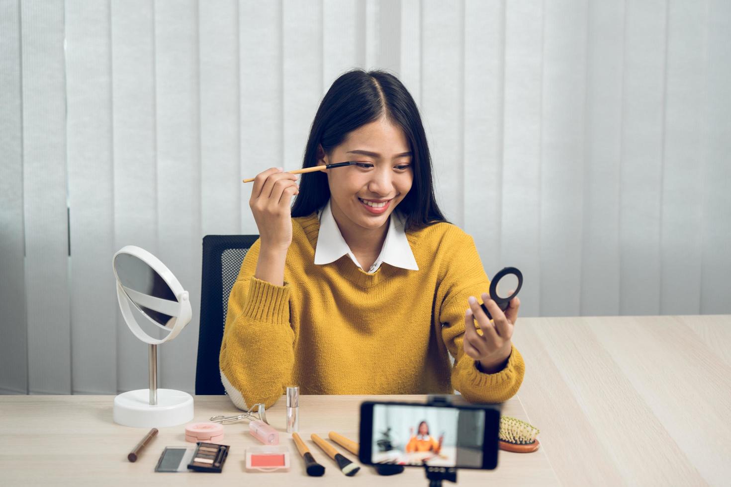 Young asian woman vlogging herself about beauty products with making a video for her blog on cosmetics using phone camera at home. photo