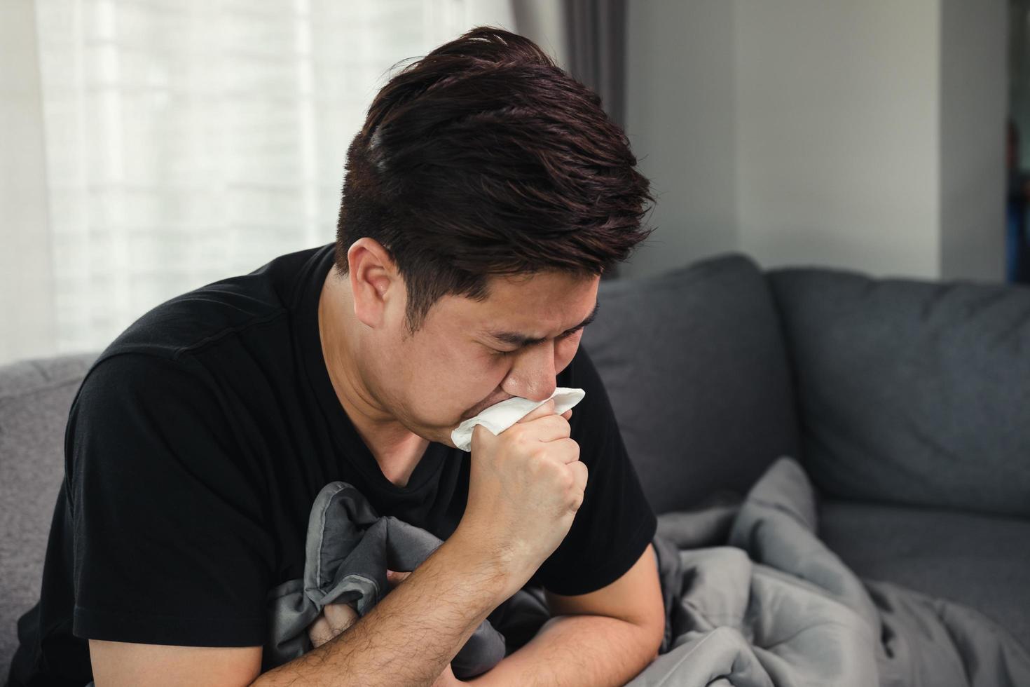 Asian people are sick or ill with bronchitis while coughing by covering their mouth with tissue paper when he sit on the sofa at home. photo