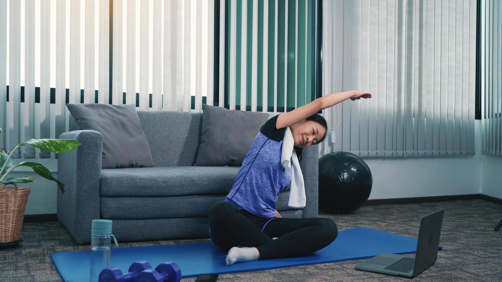 Asian woman stretching during a yoga class with a trainer at her laptop computer at home. photo