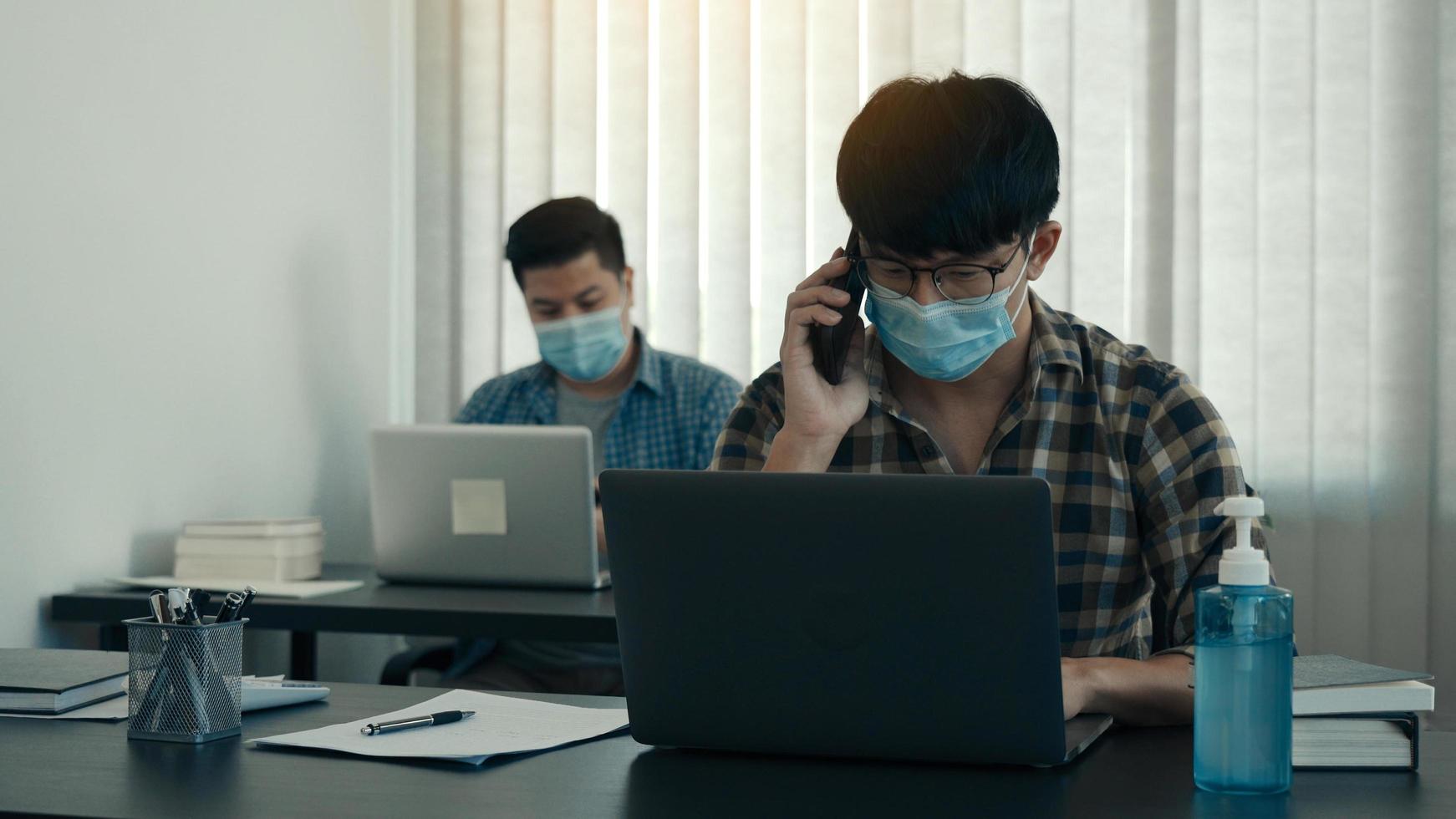 Asians sit in their office and use the phone to talk to clients while wearing masks in their offices during COVID-19. photo