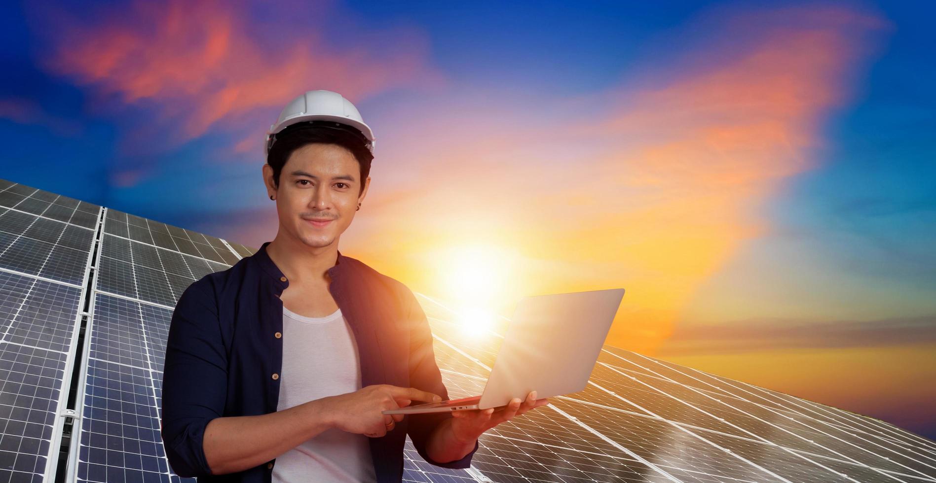 Asian man engineer white helmet holding a Laptop works in the energy solar base. photo