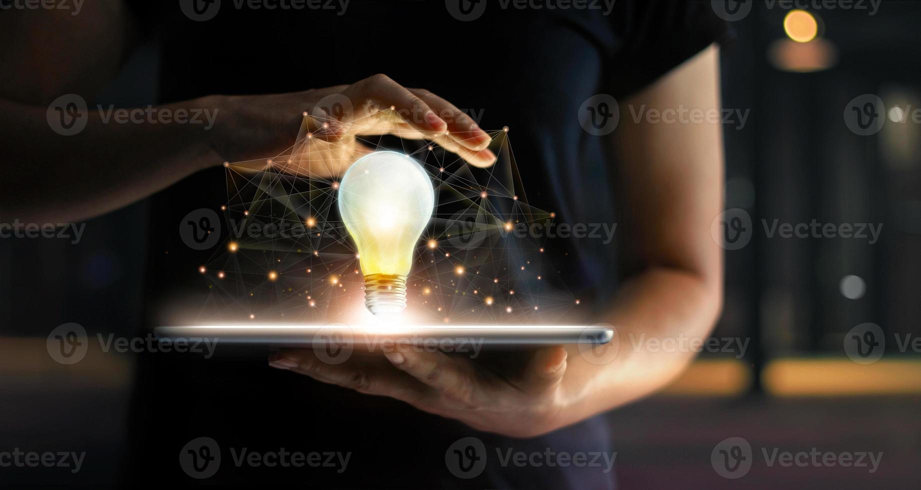 Innovation concept. Hands holding tablet and illuminated light bulb with global network connection on screen, Technology and communication on dark background. photo