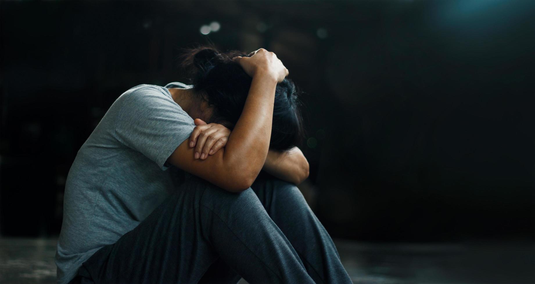 PTSD Mental health concept. Post Traumatic Stress Disorder. The depressed woman sitting alone on the floor in the dark room background. Film look photo