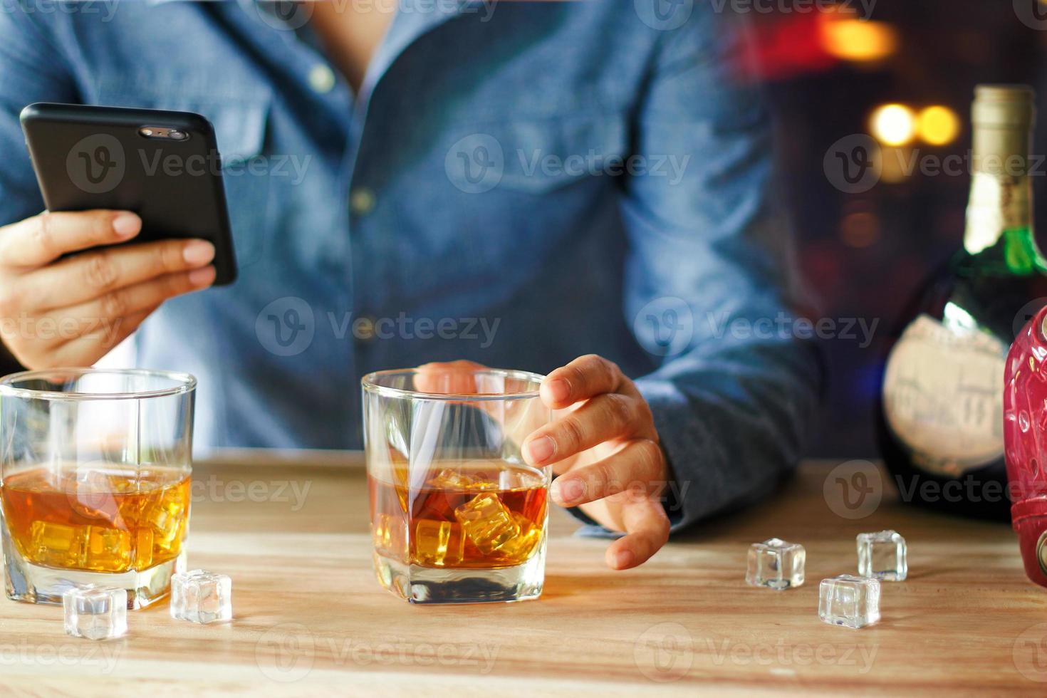 hombre que usa un teléfono inteligente mientras bebe whisky bebida alcohólica en el mostrador del bar en el pub foto