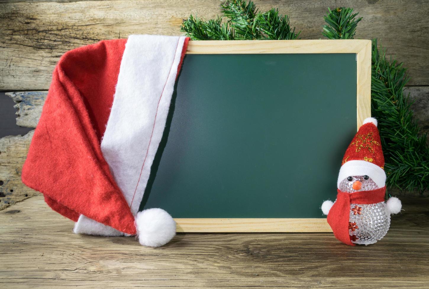Blackboard With Red Santa Hat And Christmas snowman toy on old wooden background. photo