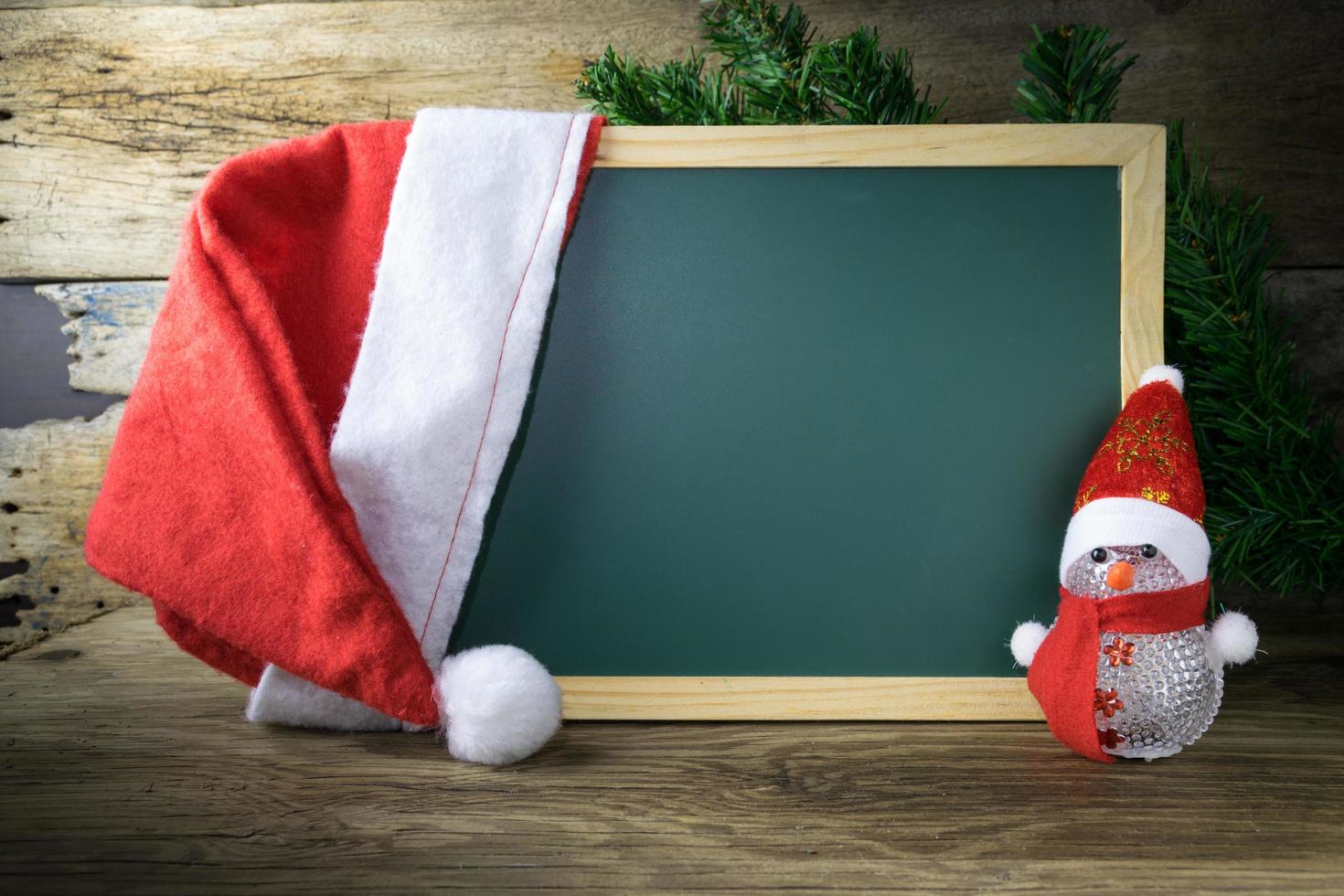 Blackboard With Red Santa Hat And Christmas snowman toy on old wooden background. photo