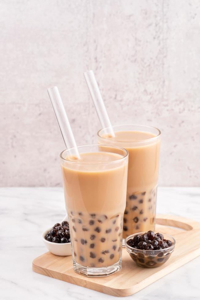 Tapioca pearl ball bubble milk tea, popular Taiwan drink, in drinking glass with straw on marble white table and wooden tray, close up, copy space. photo