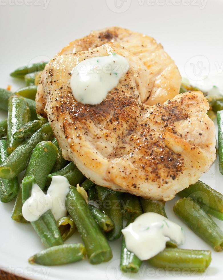 Grilled chicken breast with green beans and sauce on a white plate. photo