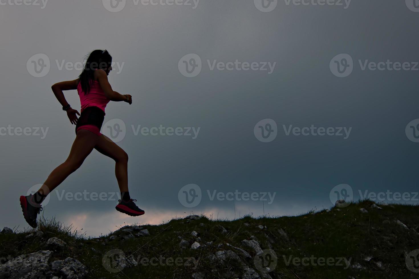 Sporty girl with beautiful athletic body runs in the alpine ridge at dusk photo