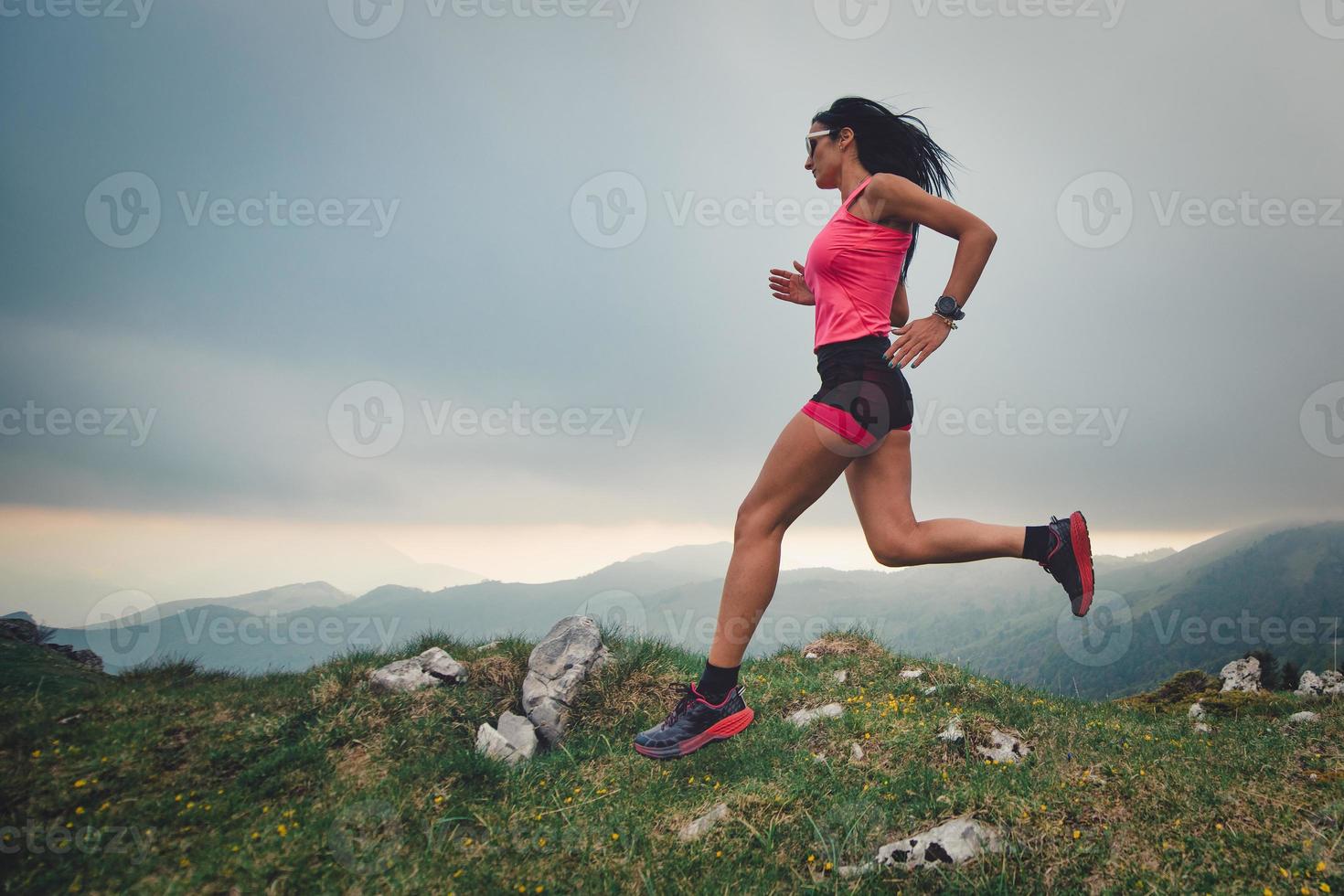Sporty girl with a beautiful body practicing trail running in the mountains photo