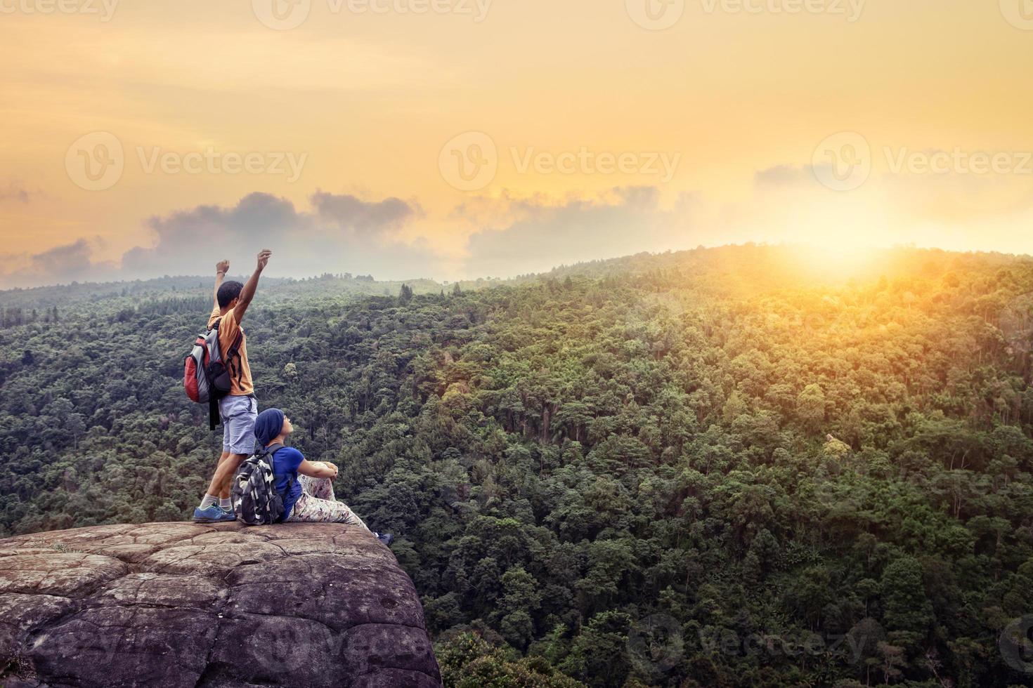 couples of traveling man and woman relax on top of  high mountain with beautiful sunset sky behind green mountain photo