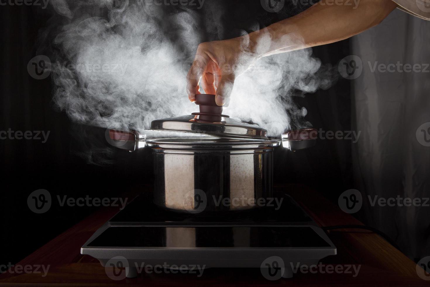sujeción manual de la tapa de la olla de metal con vapor caliente que fluye desde el interior foto