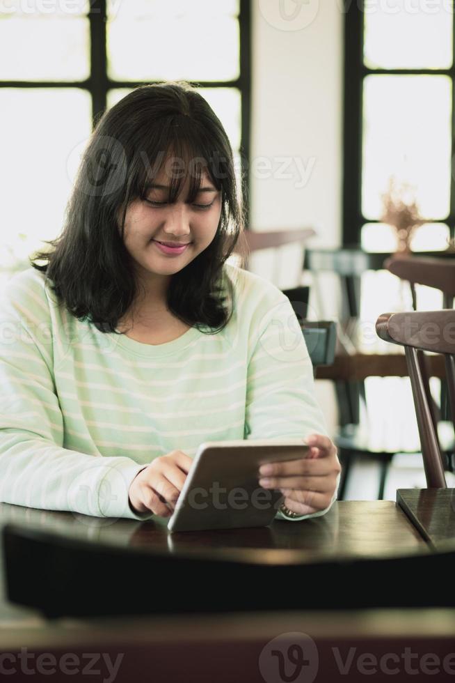 asian younger woman reading message on computer tablet with smiling face photo