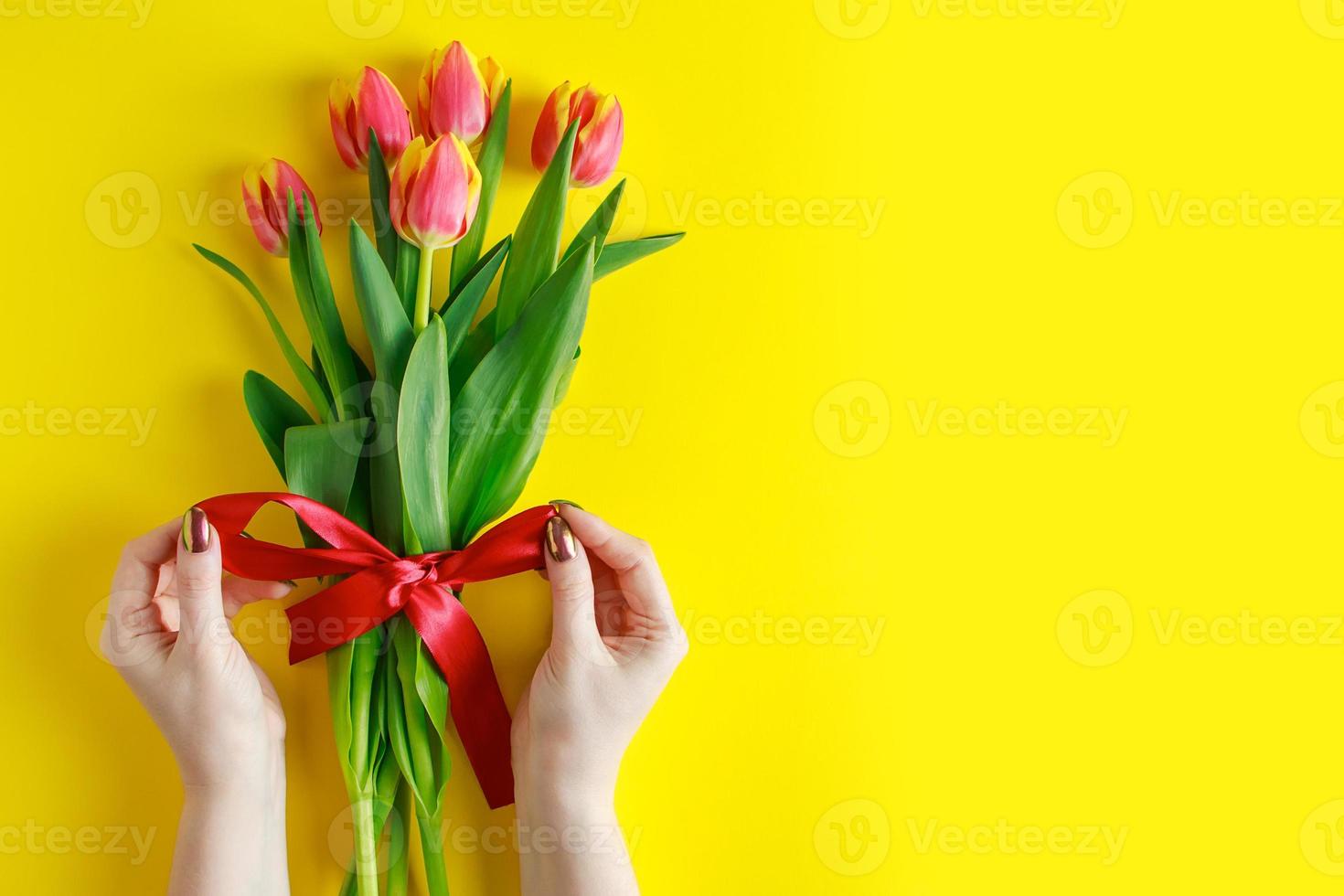 Woman ties bow on bouquet of tulips. Colorful fresh spring flowers on yellow background. photo
