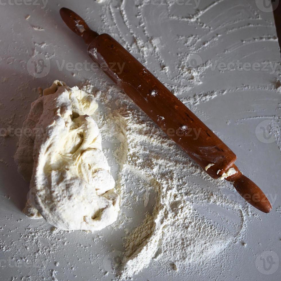 Wooden rolling pin with white wheat flour on the table photo