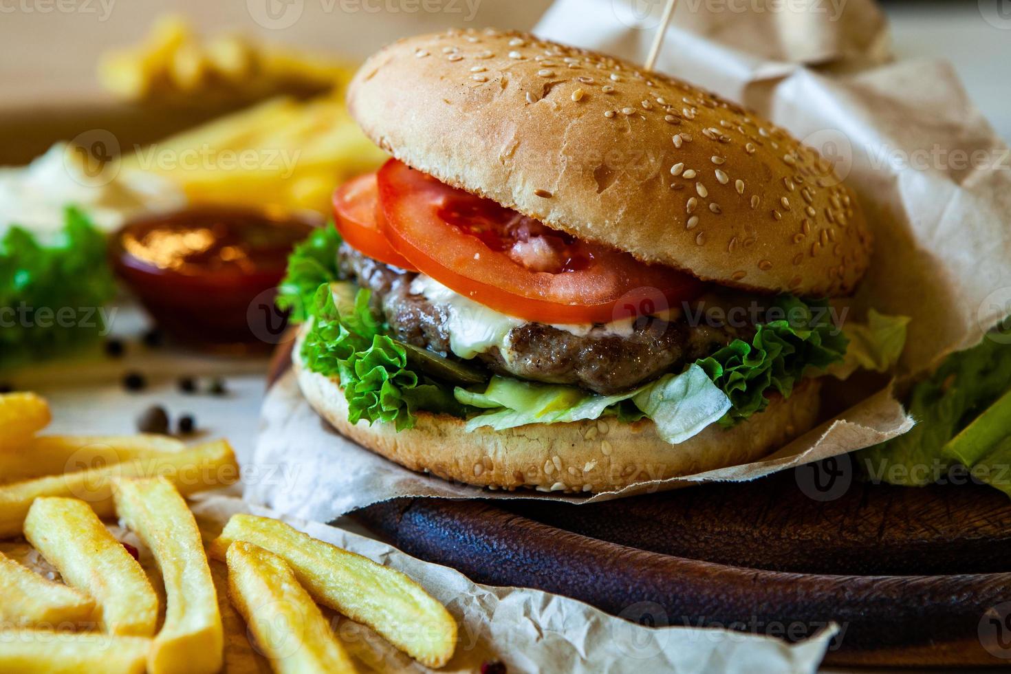 big tasty burger on a wooden table and french fries. Delicious burger with beef, tomato, cheese and lettuce. photo