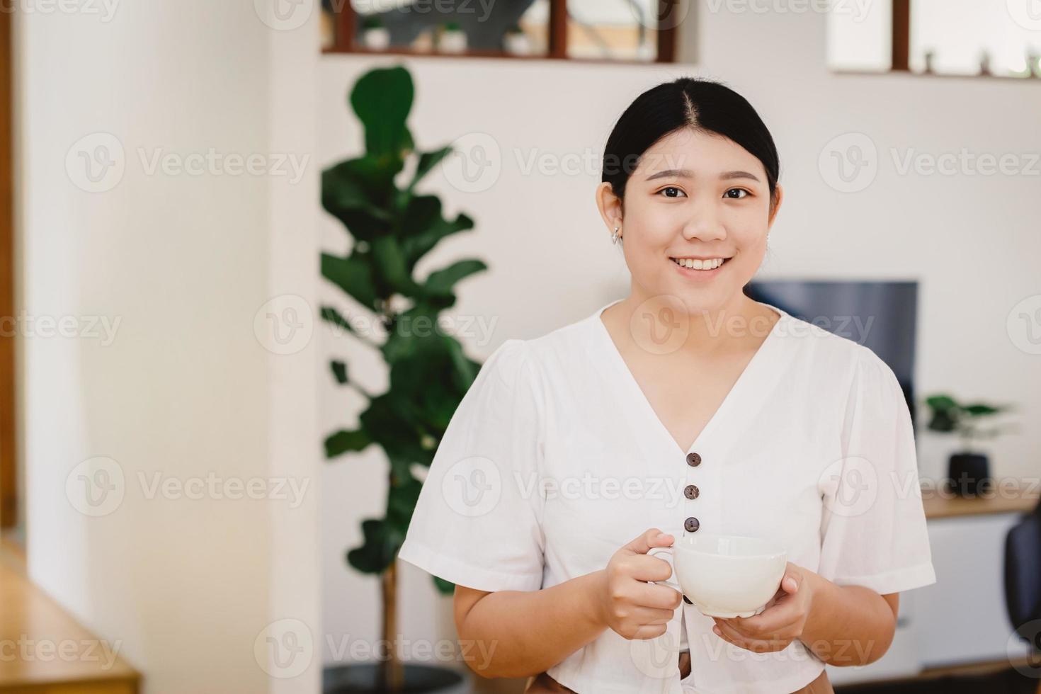 una linda adolescente asiática maneja una taza y sonríe para hacer dieta bebiendo té de hierbas o una bebida saludable en casa. foto