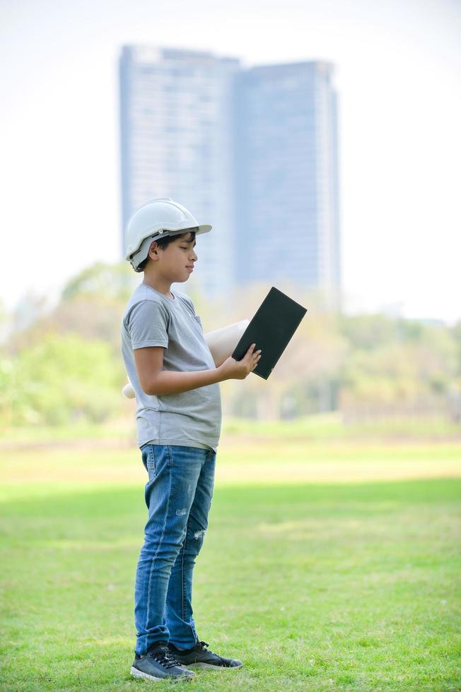 un niño medio indio tailandés con casco sostiene un plano y espera que en el futuro sea un ingeniero para construir edificios foto