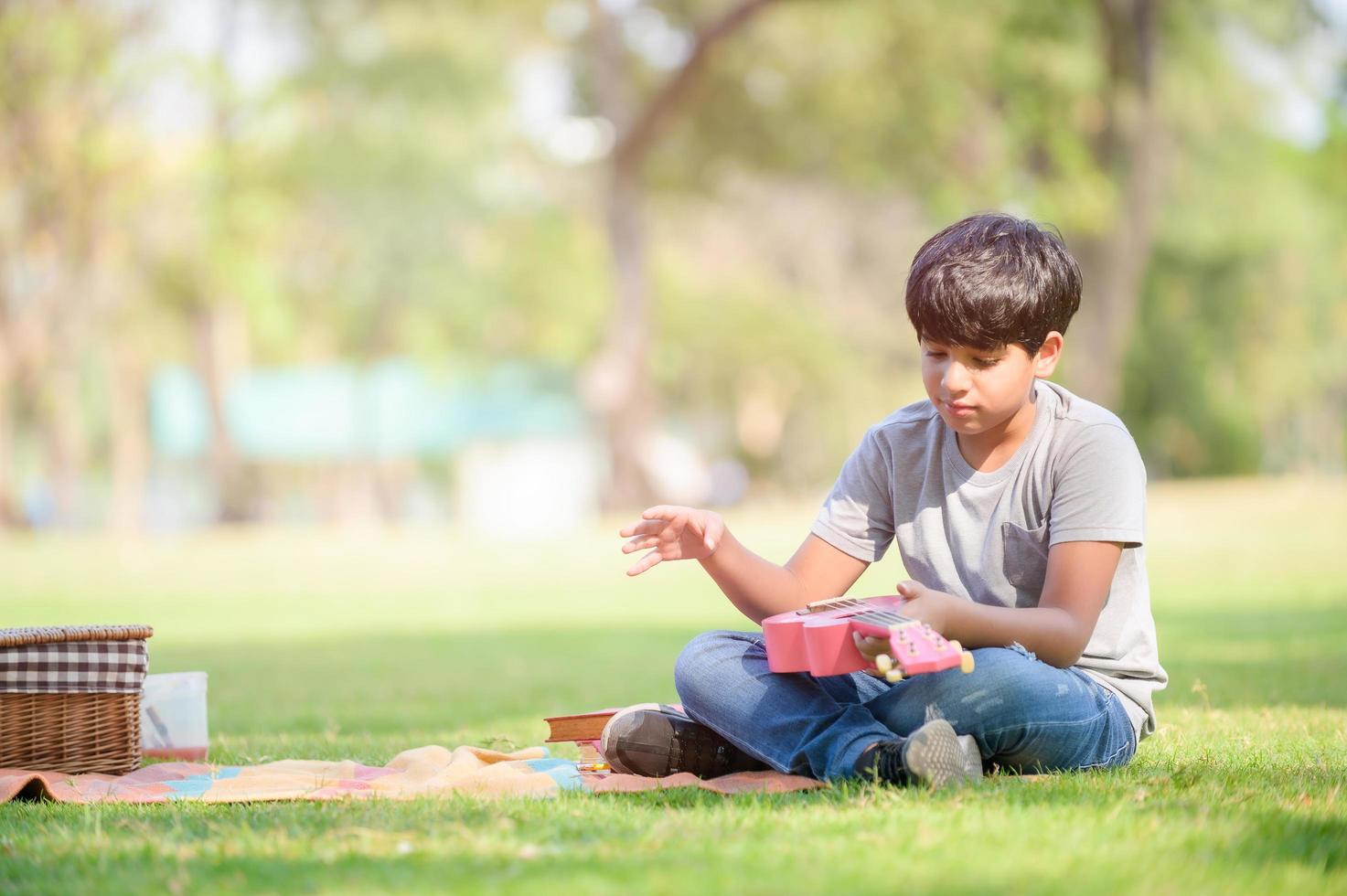 un niño mitad indio tailandés se relaja aprendiendo a tocar cuerdas de ukelele mientras aprende fuera de la escuela en un parque foto