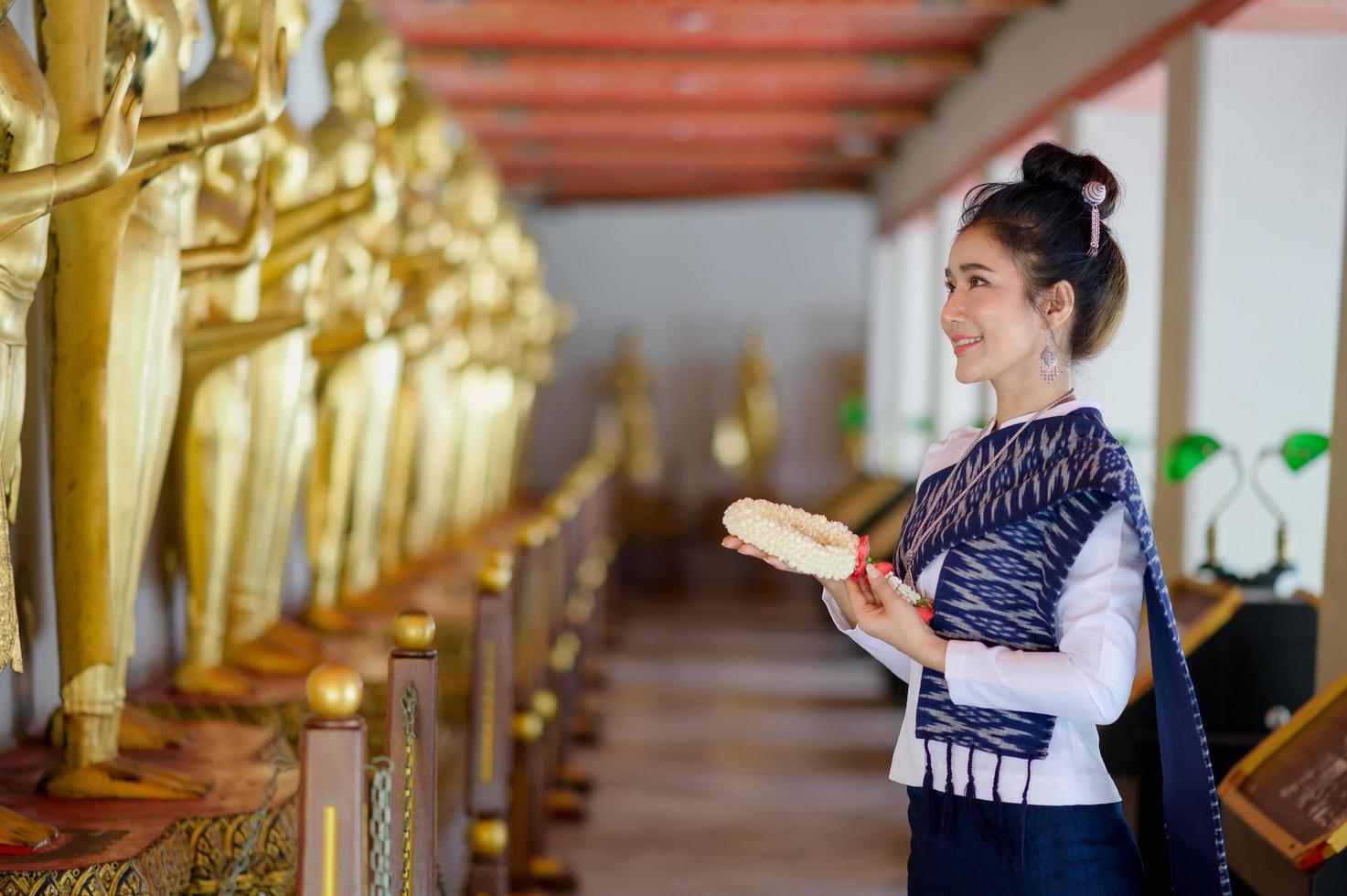 Hermosas mujeres tailandesas con vestimenta tradicional tailandesa usan guirnaldas de flores frescas para rendir homenaje a la imagen de buda, para pedir un deseo en el festival tailandés de songkran foto