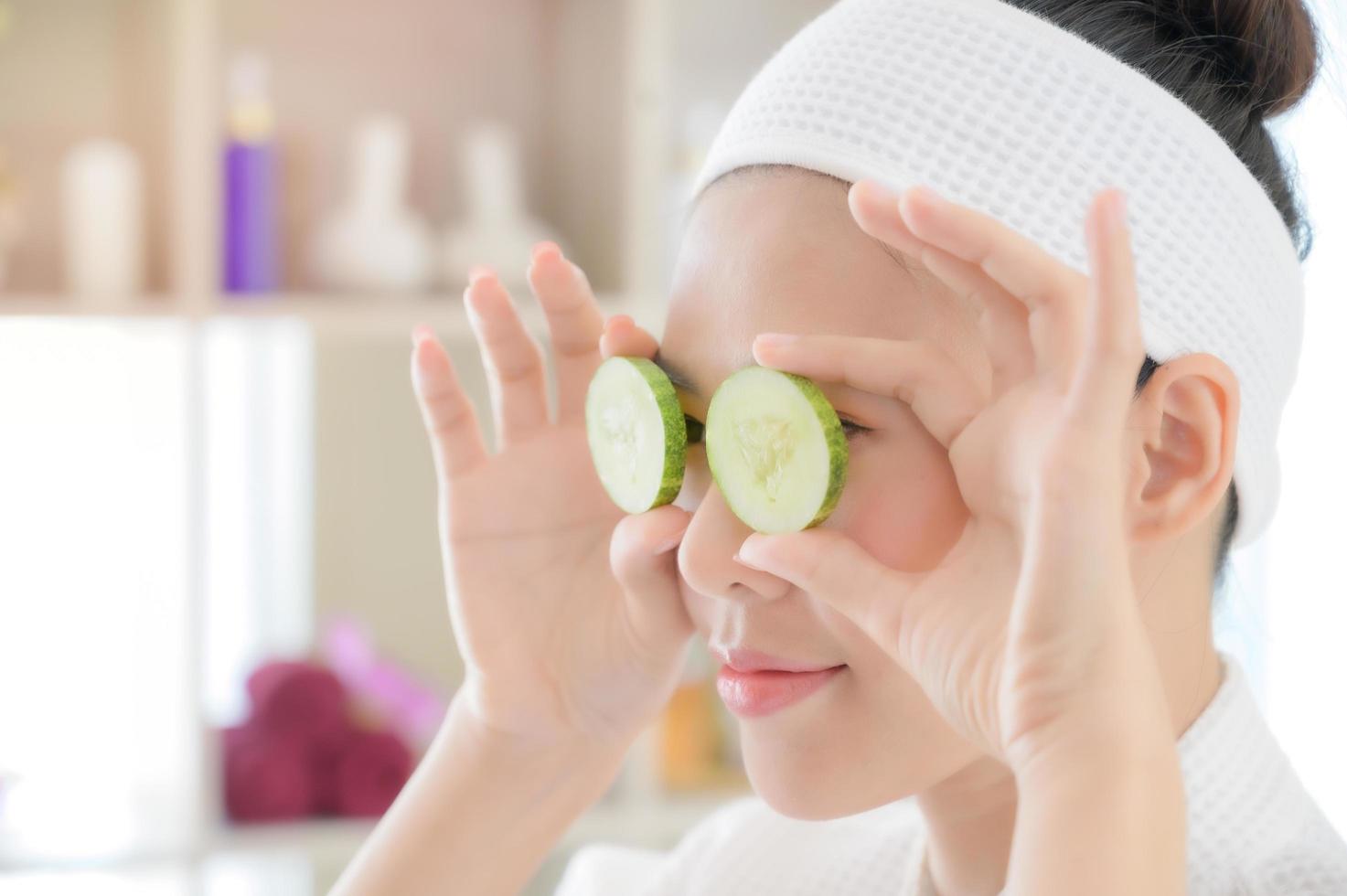 una hermosa mujer asiática usa pepino para el tratamiento facial, junto con un masaje de una masajista profesional en el salón de spa foto