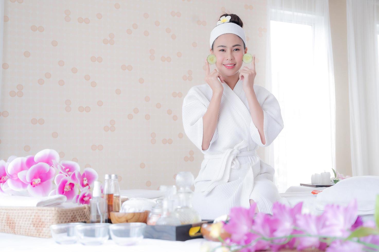 una hermosa mujer asiática usa pepino para el tratamiento facial, junto con un masaje de una masajista profesional en el salón de spa foto