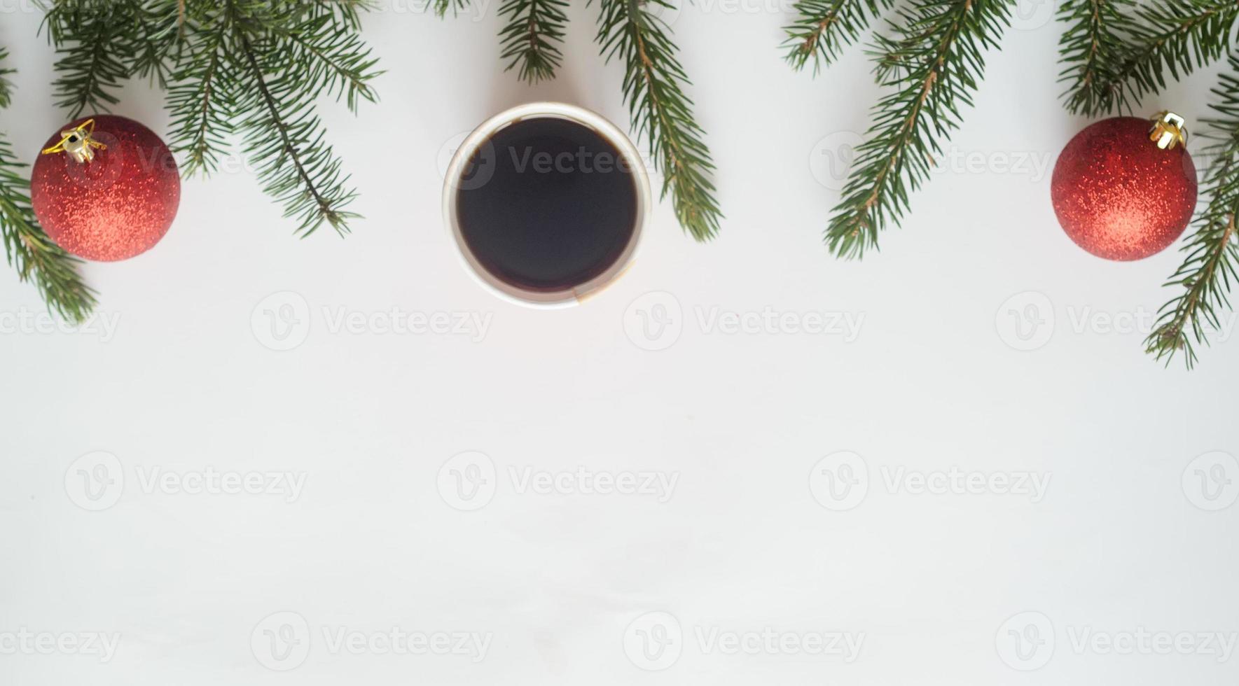 café de navidad. vista superior, una taza de café y dos bolas rojas con ramas de árboles de navidad sobre fondo blanco, copyspace en la parte inferior. foto