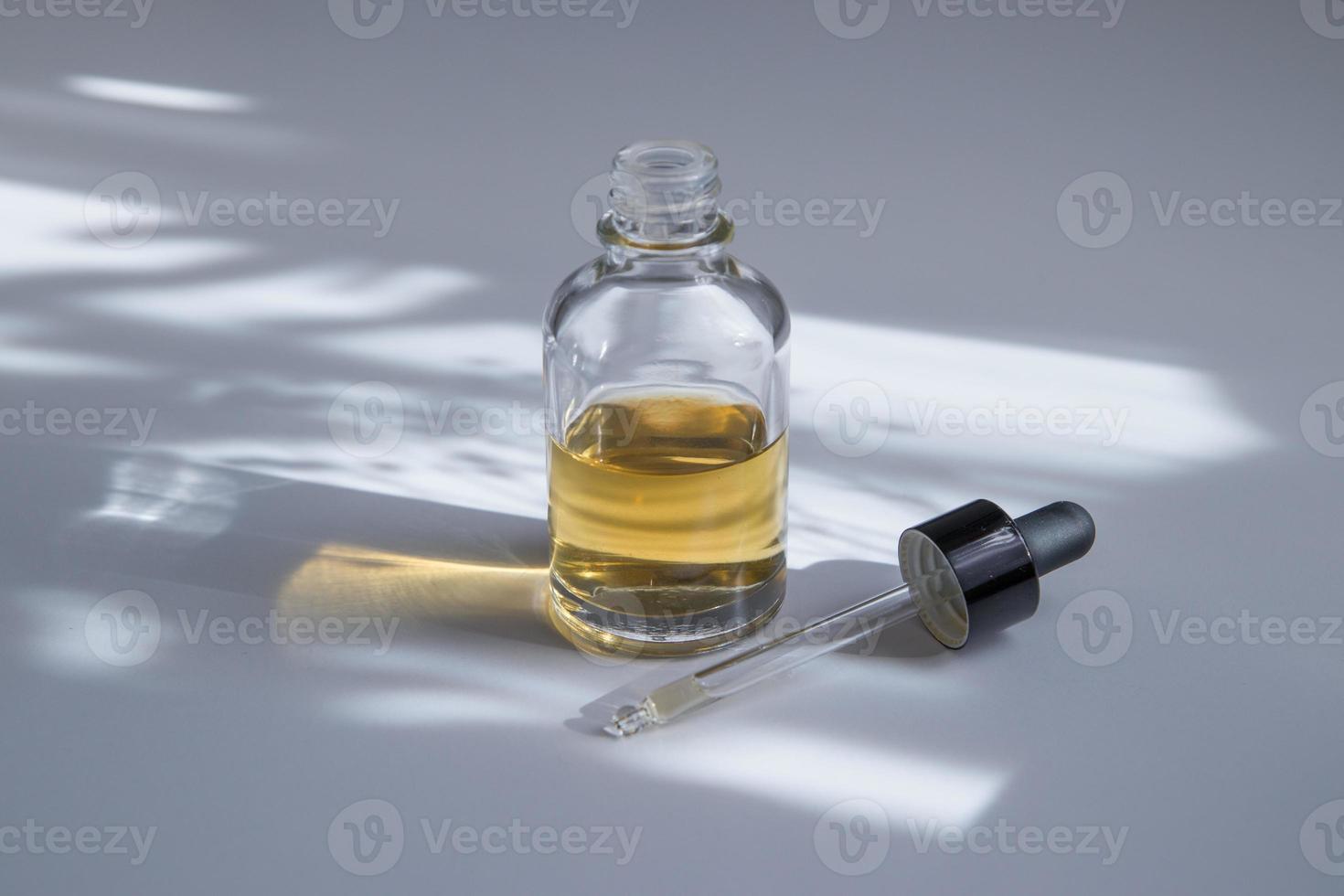 frasco cuentagotas de vidrio abierto con cosmético para el cuidado de la piel. mantequilla, suero o tintura con sombra dura foto