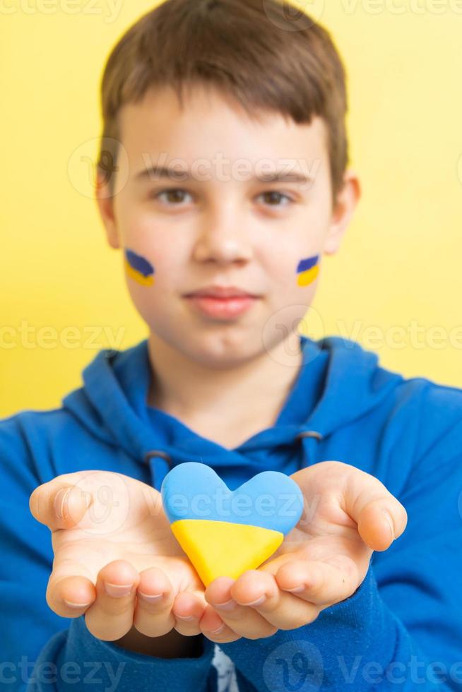 corazón de colores amarillo y azul de la bandera ucraniana en manos de un niño. enfoque variable. formato vertical foto