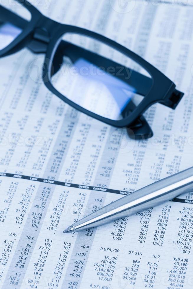 Pen and glasses rest on stock price detail financial newspaper photo