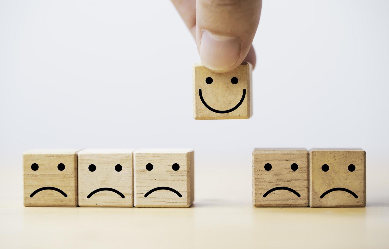 Hand holding Smile face print screen on wooden cube block among sadness face for customer service evaluation and emotion mindset concept. photo