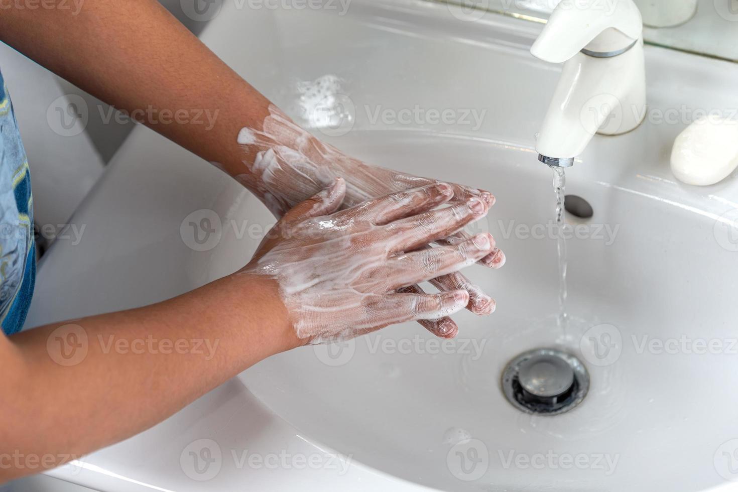 mujer lavándose las manos con espuma de jabón y agua del grifo en el baño. limpie a mano bajo el grifo del fregadero para la higiene personal para prevenir la gripe y el coronavirus. buen procedimiento de lavado de manos para matar bacterias, virus foto