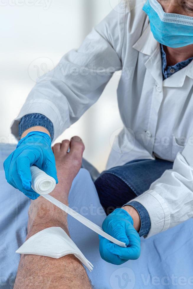 Wounded man's leg hurts. Patient receiving a first aid. Nurse bandaging a wound. photo