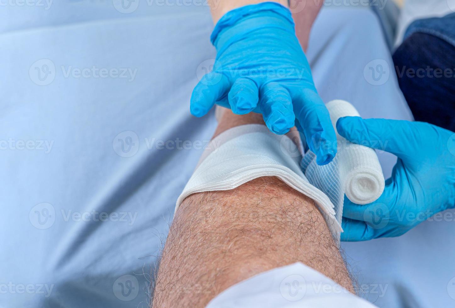 Wounded man's leg hurts. Patient receiving a first aid. Nurse bandaging a wound. photo